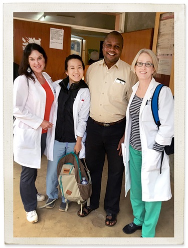 Three women in white coats and one man stand and smile at the camera