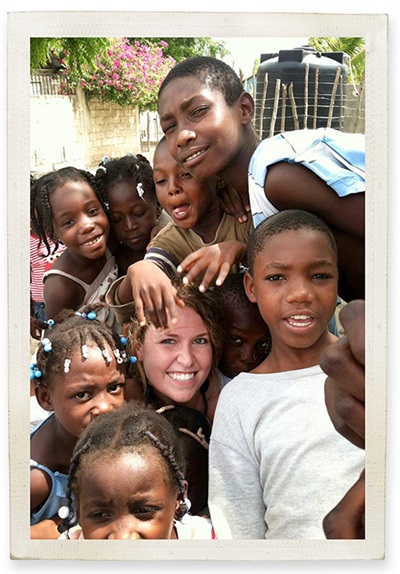 A Caucasian woman's face is surrounded by the faces of dark-skinned children