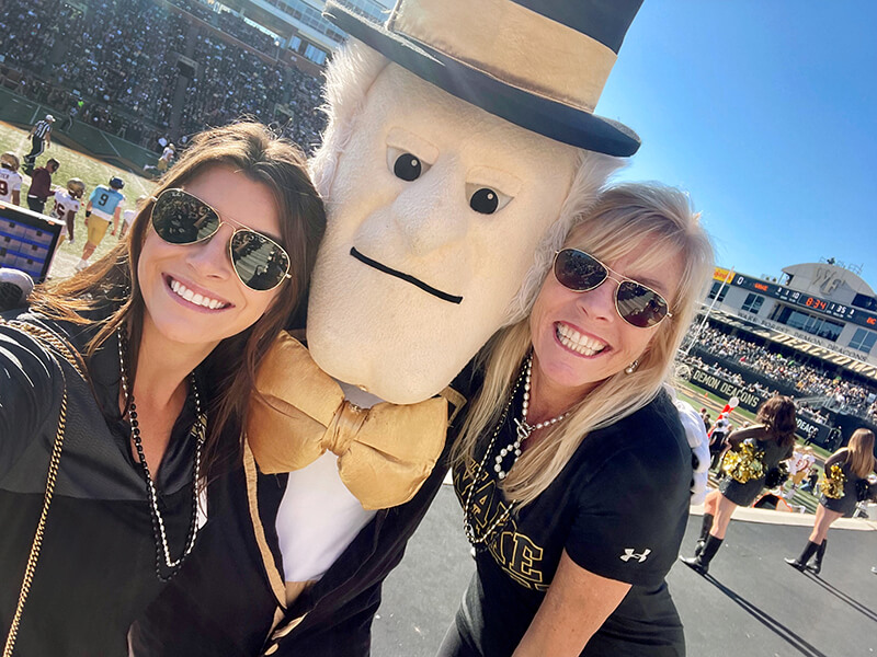 Two women standing next to the Demon Deacon and smiling at the camera.