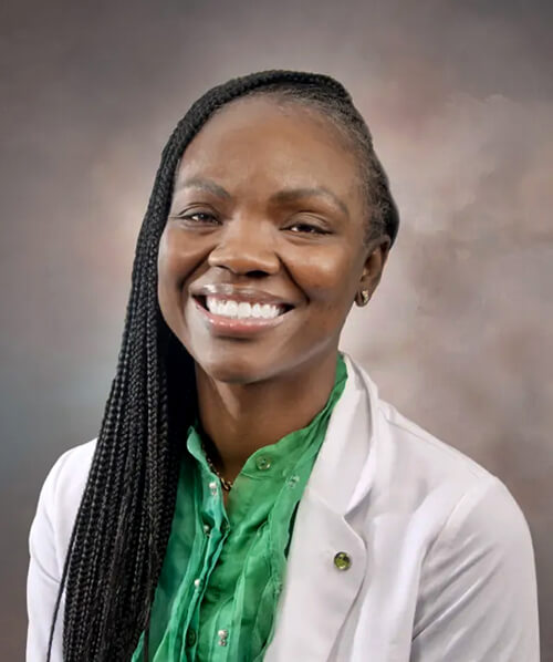 A woman wearing a green shirt and a lab coat smiling at the camera.