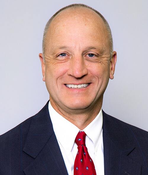 A man wearing a suit and red tie smiling at the camera.