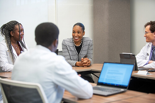 A young woman sitting at a table with three people wearing lab coats.