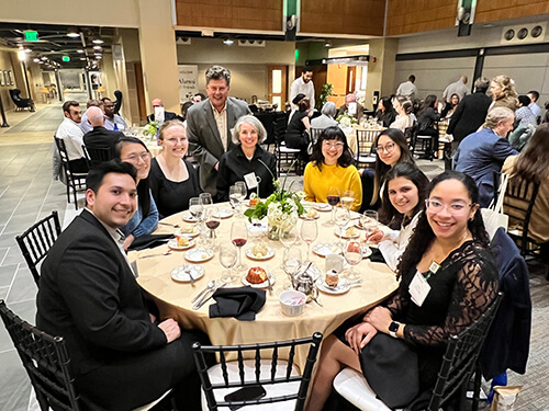 A group of young people sitting around a table and smiling at the camera.