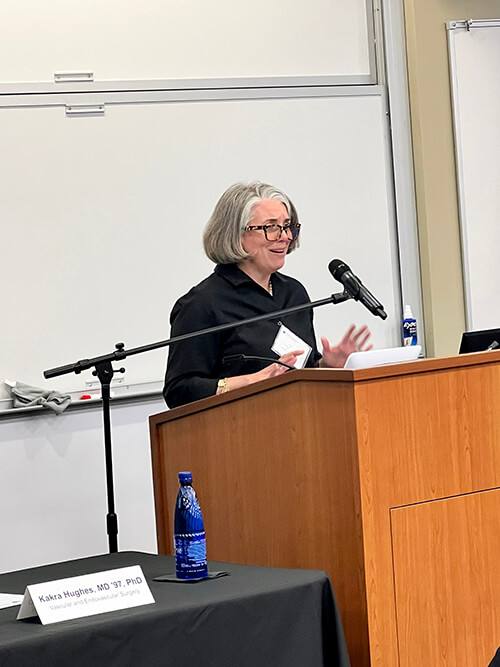 A woman wearing a long-sleeved black shirt speaking at a podium.