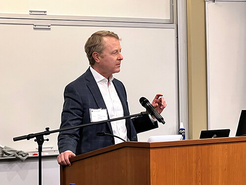 A man wearing a black jacket speaking at a podium.