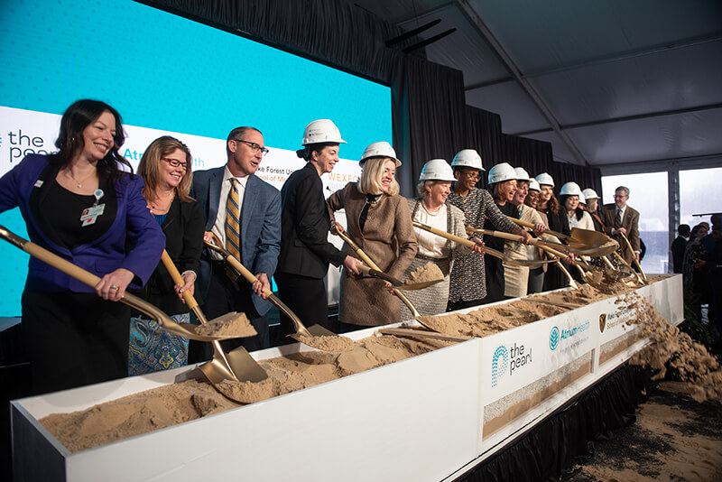 A group of people shoveling dirt at a groundbreaking ceremony.