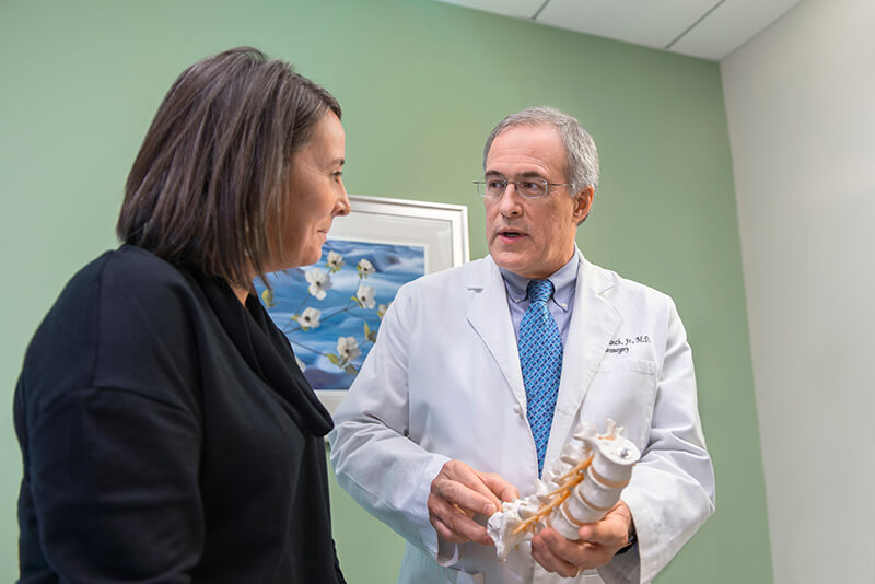 A medical professional speaking while holding a spine model.