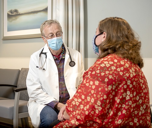 An older male doctor wears a mask while talking with a patient