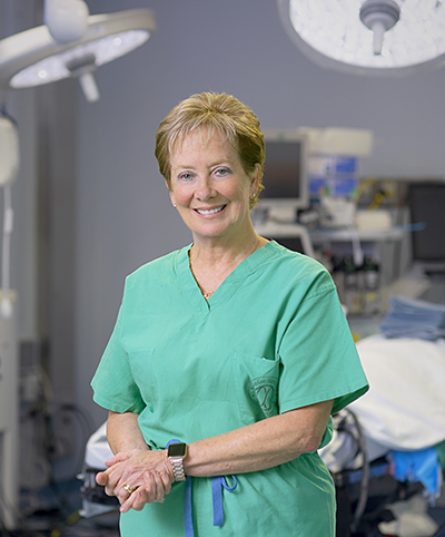 Caucasian woman with strawberry-blonde hair wearing surgical scrubs stands in the operating room