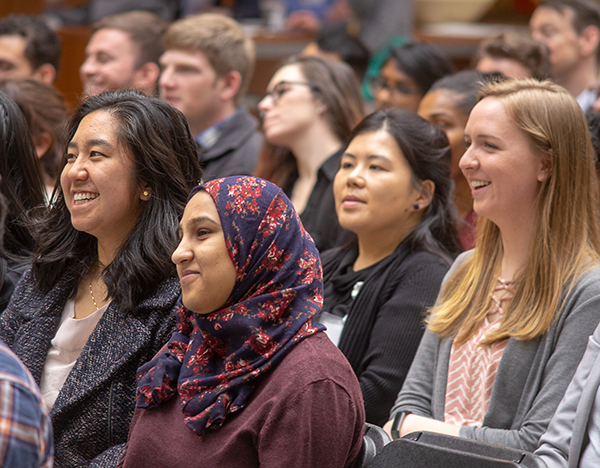 Group of diverse female students sit in an assembly, smiling at the speaker