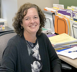 Smiling woman with curly brown hair smiles as she sits at her desk