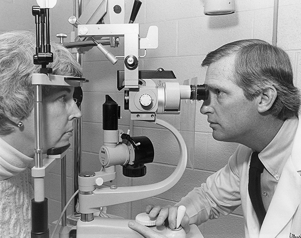 Black and white photo of a white man looking through optical equipment