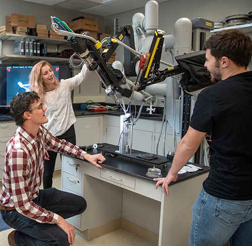 Graduate students stand around and discuss a surgery machine