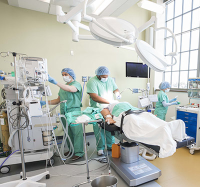 People in surgical scrubs surround a mannikin in a mock surgical suite
