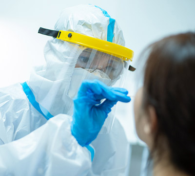 Gowned, gloved and masked health care worker in a face shield does a nasal swab on a dark-haired female