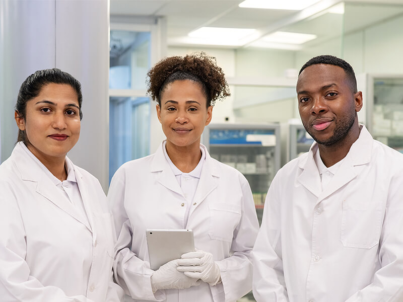 Two women and one man all wearing white lab coats, smiling.