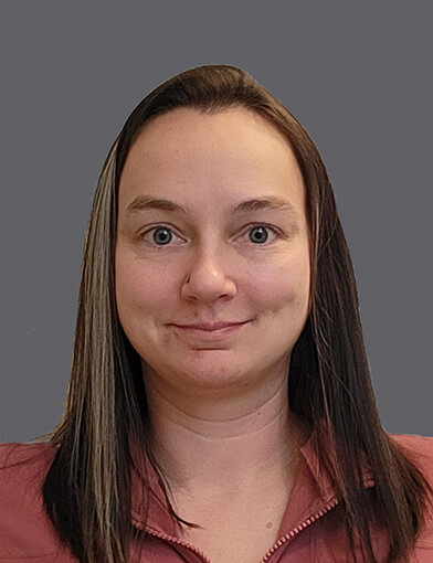 A woman with long brown hair, wearing a brown shirt and smiling at the camera.