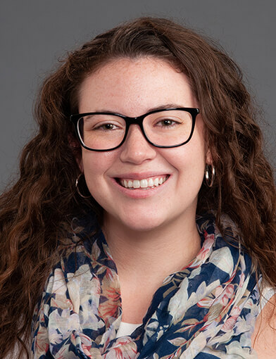 A woman with curly brown hair, wearing glasses and smiling at the camera.