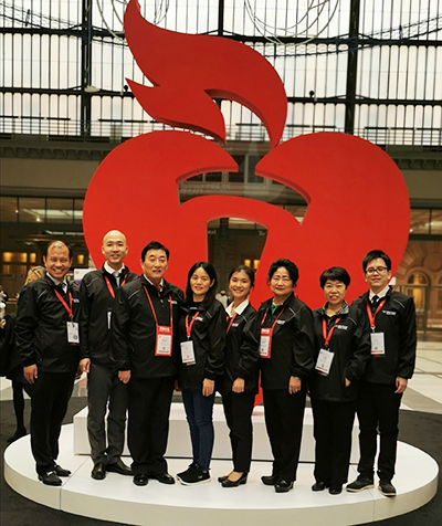 a group of men and women, all wearing black, stand in front of a large red heart symbol