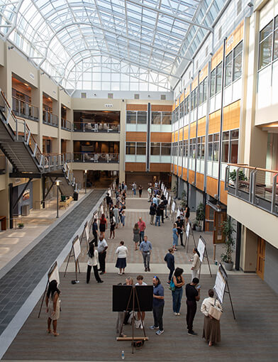 A large atrium with numerous large posters spread throughout the room and people standing to look at them.