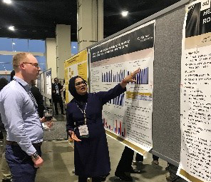 A woman points out something on a research poster to the man standing in front of her looking at the poster