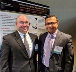 Two men in suits stand in front of a research poster