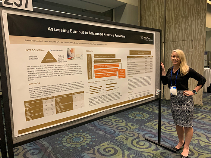 A blonde woman stands beside a presentation poster