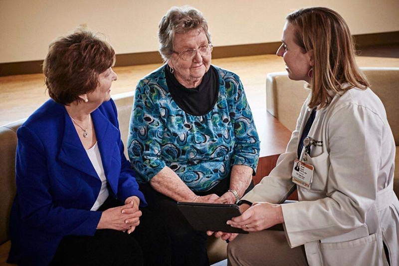 A younger woman in a white coat talks with two older women