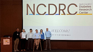 Six people standing on stage in front of a screen that reads "NCDRC North Carolina Diabetes Research Center".