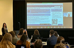 A person standing in front of a screen, giving a presentation to a crowded room.