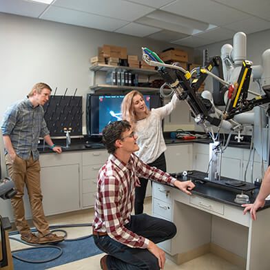 A group of men and women working on a robotic arm in a lab.