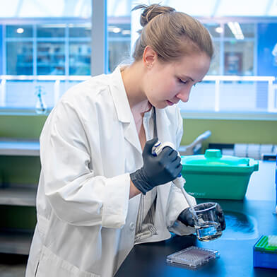 A young woman in a white lab coat putting samples into a dish.