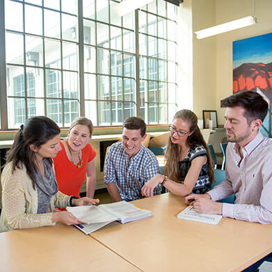 A group of young men and women sitting at a table and talking to each other.
