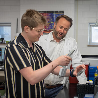 A young man looking at some science equipment while a professor looks on.