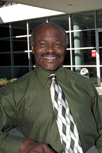 An older man wearing a green shirt smiling at the camera.