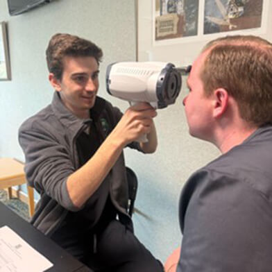 A young man pointing a medical measuring device at another man in a gray shirt.