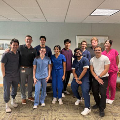 A group of young men and women in scrubs of various colors smiling and standing next to each other.