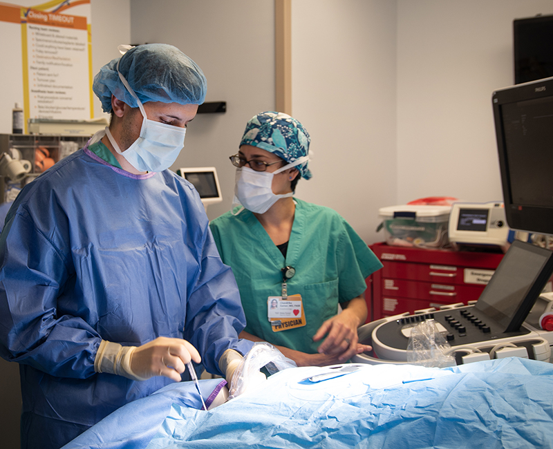 A blue gowned person operates on a blue-draped object in an OR