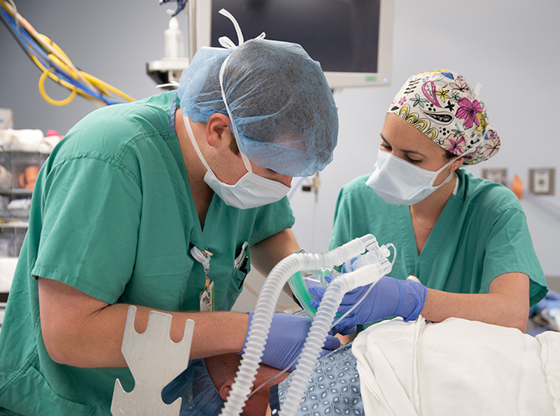 Two people in green scrubs monitor anesthesia in an OR