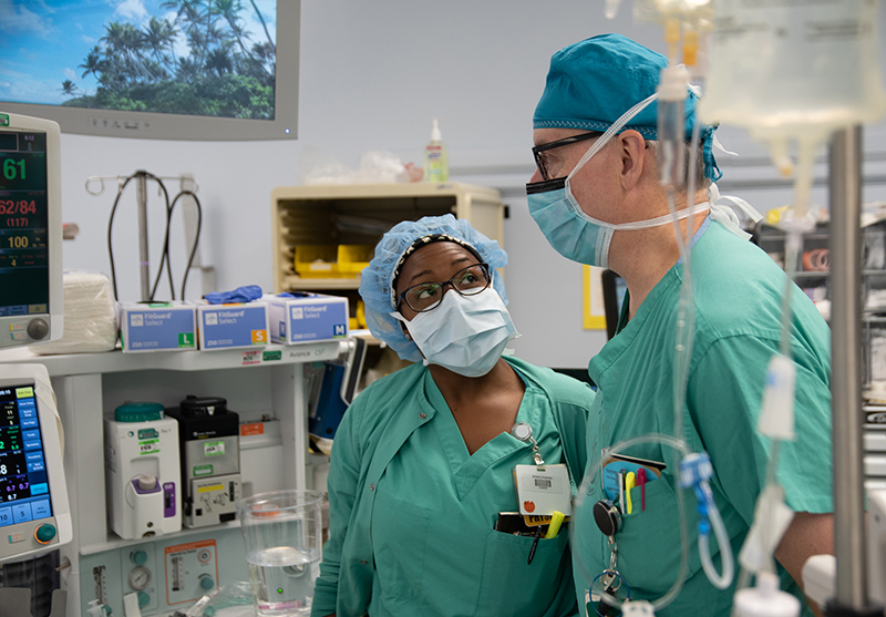 Two people in green scrubs talk in an OR