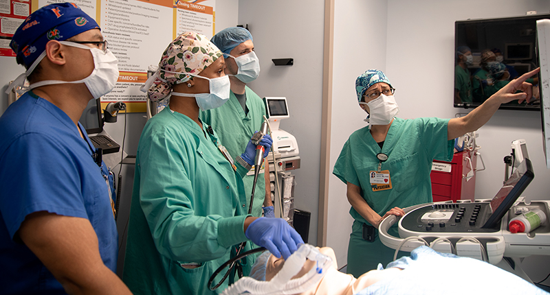 Four people in scrubs gather around and practice on a simulation mannikin