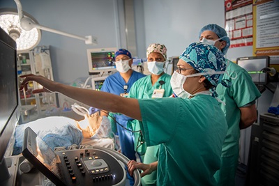 Surgical team in full scrubs in operating room monitors an unconscious patient's breathing