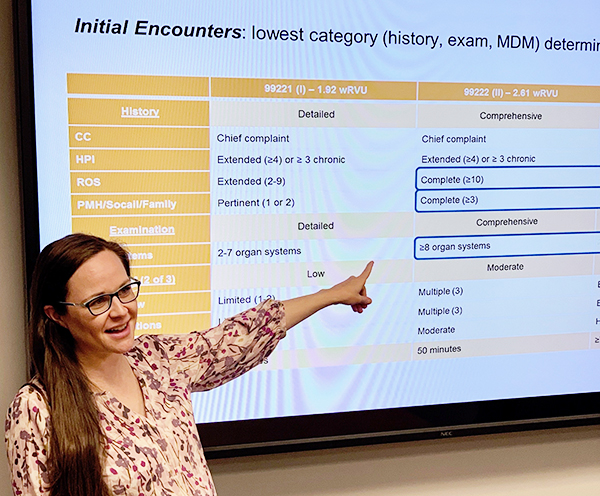 A woman with long dark hair points to a field displayed on a projection screen