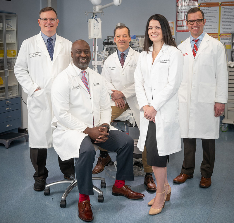 Four men and one woman, all wearing white coats, smile at the camera