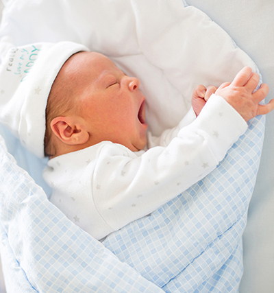 Baby boy dressed in blue and white outfit yawns in his sleep