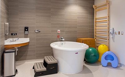 Large, modern delivery room with large birth tub, balance ball, wall stretching rack and other assorted equipment