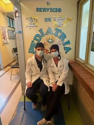 Two medical professionals wearing scrubs and face masks looking at the camera.