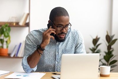 Serious African-American employee making business call focused on laptop at workplace