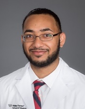 Young African American man with close-cropped beard and mustache, wearing glasses and a white coat