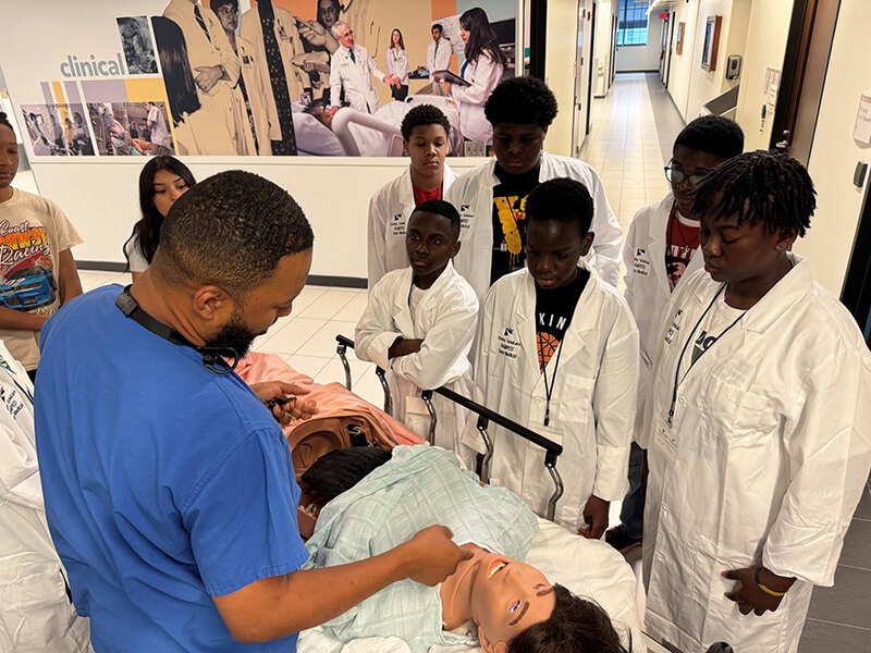 A group of people wearing lab coats looking at a medical manikin.